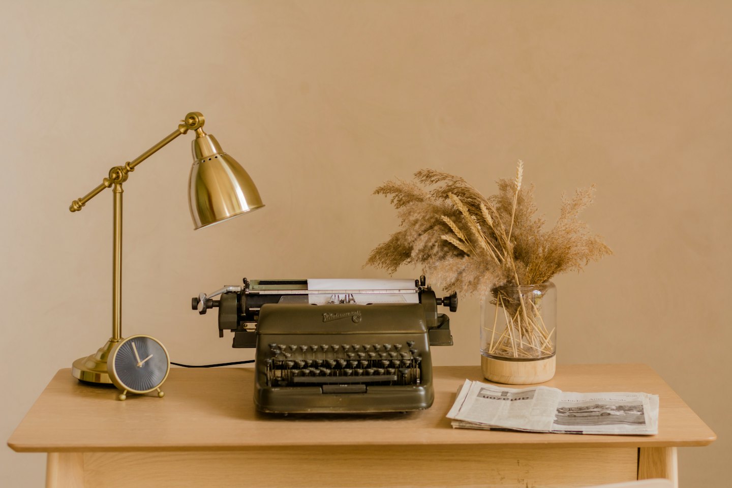 Olive green typewriter sits on a desk with a lamp.