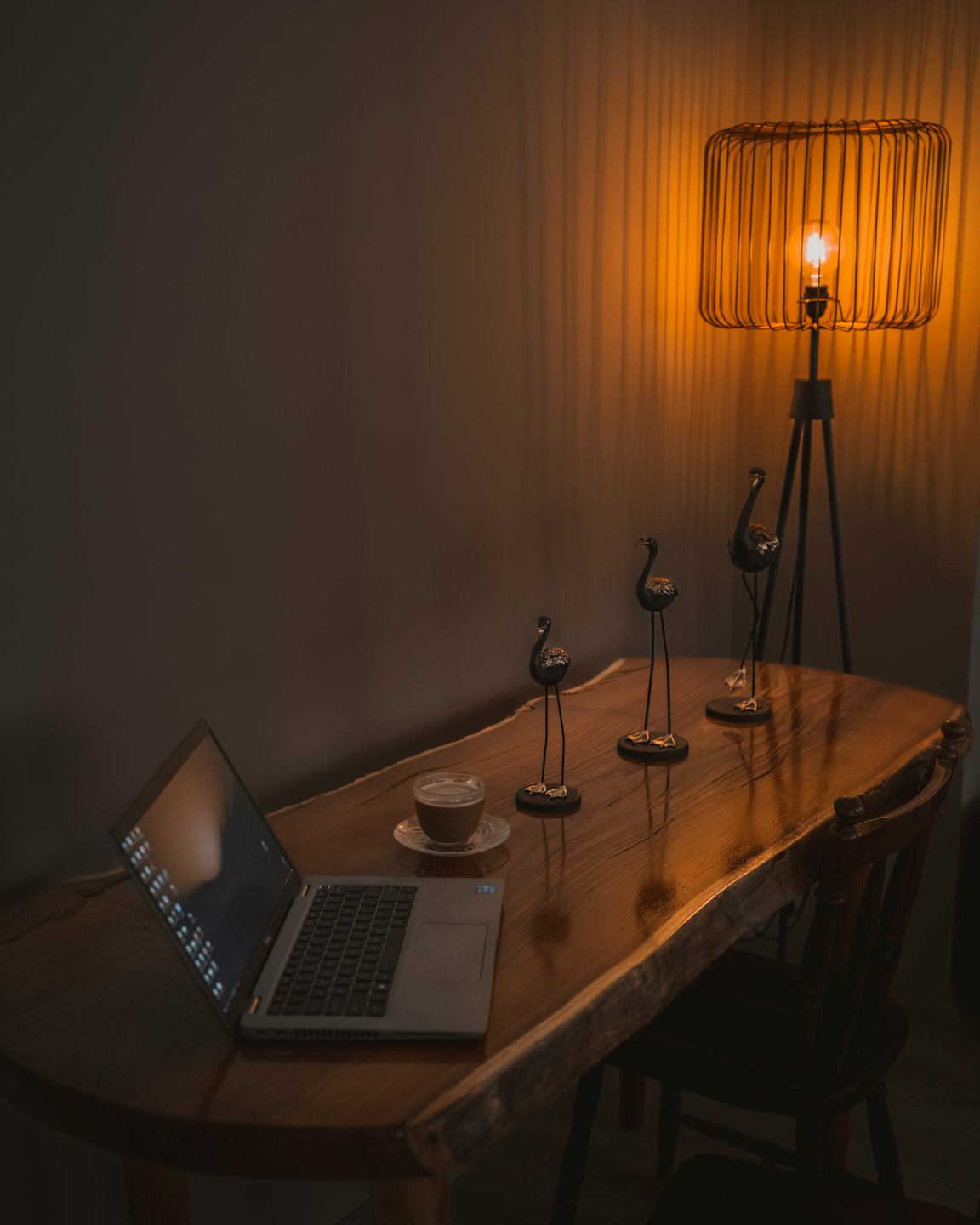 Laptop and coffee on a wooden desk with bird figurines.