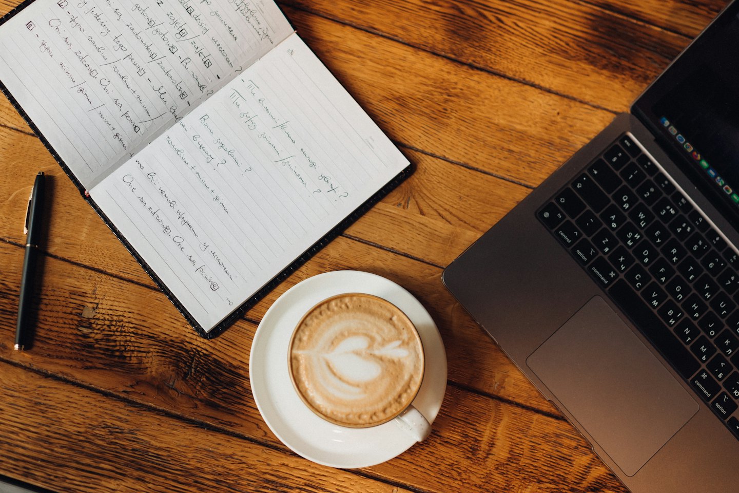 Laptop, notebook, and coffee on a wooden desk.